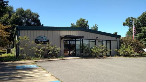 A single-story building with large windows, surrounded by greenery, and an American flag in the background.