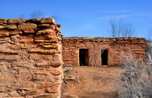 Historic adobe structure with two doorways, surrounded by dry grass and a clear blue sky.