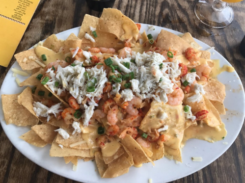 A plate of nachos topped with shrimp, crab, cheese sauce, and green onions on a wooden table.