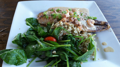 A plate featuring grilled fish with shrimp sauce, rice, and a side of fresh spinach salad with cherry tomatoes.
