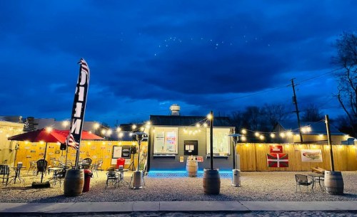 A cozy outdoor dining area with string lights, flags, and a food truck, set against a twilight sky.