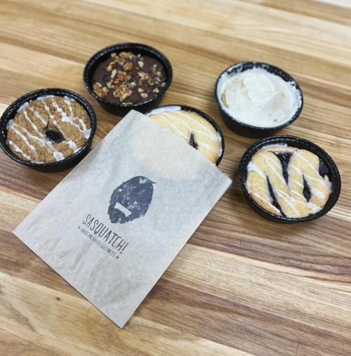 A paper bag with a Sasquatch logo, surrounded by four dessert cups on a wooden table.