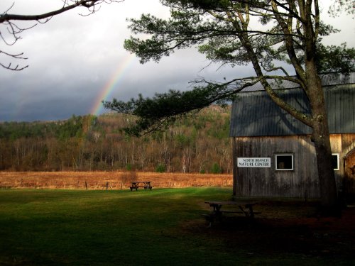 A rustic nature center building with a rainbow in the sky, surrounded by green fields and trees.