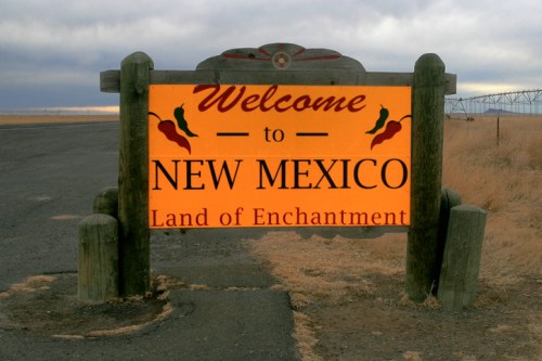Welcome sign for New Mexico, featuring "Land of Enchantment" and decorative chili peppers.