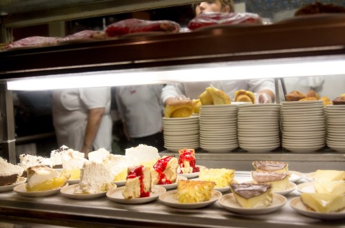 A display of various desserts on plates, including cakes and pastries, with staff in the background.