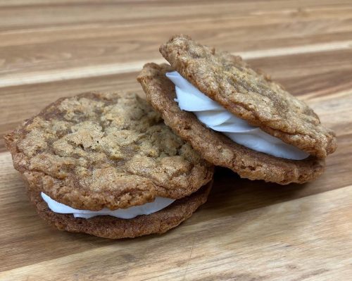 Two oatmeal cookies with white cream filling stacked on a wooden surface.
