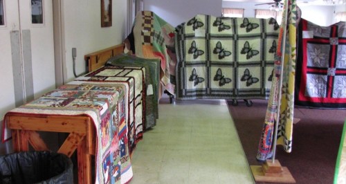 A hallway displaying various colorful quilts draped over tables and stands.