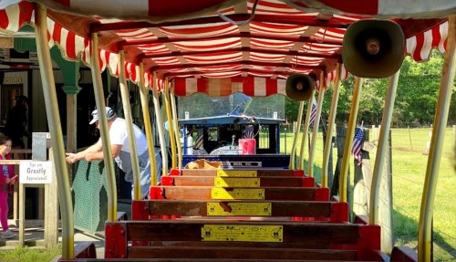 View from inside a colorful train car, with striped canopy and empty seats, at a scenic outdoor location.