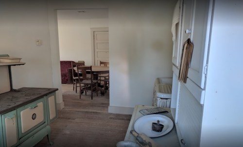 A vintage kitchen with a stove, sink, and a view of a dining area with wooden chairs and a table.