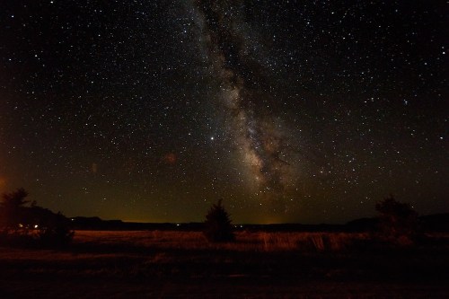 A stunning night sky filled with stars, featuring the Milky Way arching over a dark landscape.