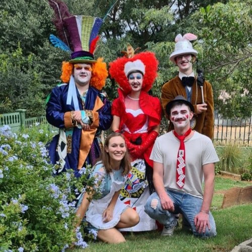 A group of five people in colorful costumes, inspired by Alice in Wonderland, posing in a garden.