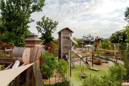 A vibrant playground featuring wooden structures, slides, and greenery under a cloudy sky.