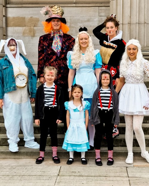 A group of people in costumes inspired by "Alice in Wonderland," posing on steps.