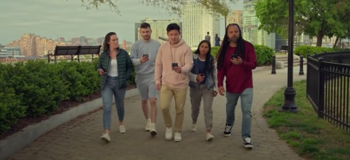 A diverse group of five people walking together in a park, each looking at their smartphones.