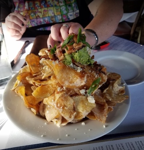A plate of crispy potato chips topped with green onions, bacon, and a dollop of guacamole.