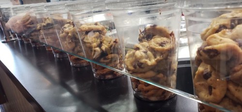 Clear containers filled with chocolate chip cookies lined up on a counter.