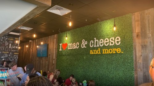 A lively restaurant interior with a green wall displaying "I ❤️ mac & cheese and more" in colorful letters.