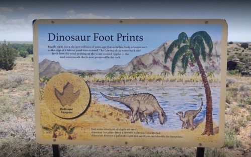 Sign displaying dinosaur footprints with a scenic background of mountains and desert, illustrating prehistoric life.