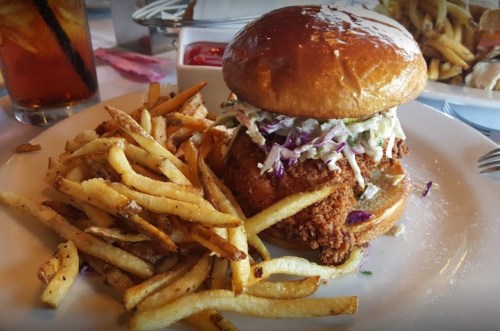A crispy fried chicken sandwich with coleslaw on a brioche bun, served with a side of golden French fries.