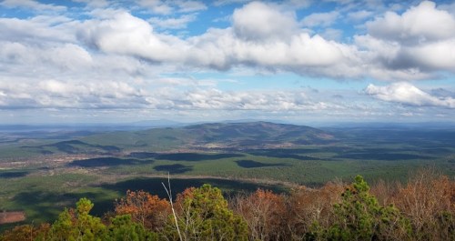 A panoramic view of rolling green hills under a blue sky with fluffy clouds, showcasing a serene natural landscape.
