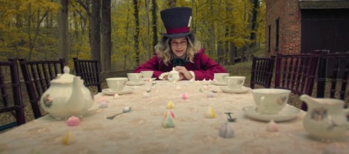 A whimsical scene with a man in a top hat at a long table set for tea in a forest, surrounded by colorful desserts.