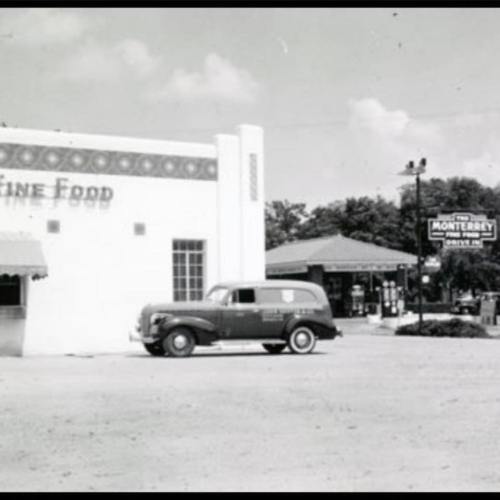 A vintage black-and-white photo of a fine food store with a classic car parked outside and a nearby sign for Monterey.