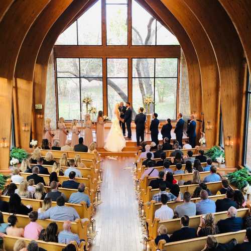 A wedding ceremony in a wooden chapel with guests seated, a couple at the altar, and large windows letting in natural light.