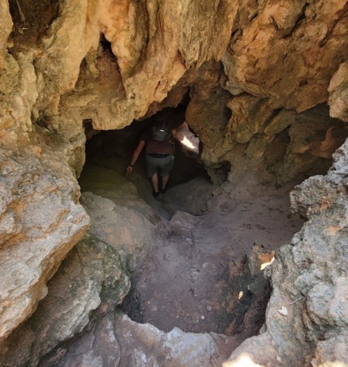 A person climbs up a rocky, narrow cave passage, surrounded by rough stone walls and dim lighting.