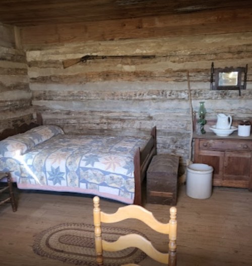 A rustic room with a bed, wooden furniture, a chair, and a vintage decor against log walls.