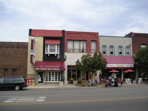 Colorful storefronts line a street, featuring a restaurant, a bakery, and an ice cream shop with outdoor seating.