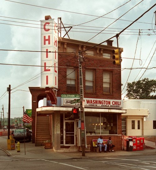 A vintage brick building with a large "CHILI" sign, housing Washington Chili, on a busy street corner.