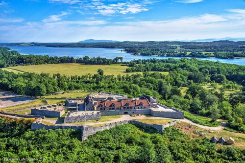 Aerial view of a historic stone fortress surrounded by lush greenery and a serene lake in the background.