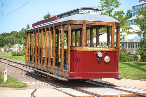A vintage red and wooden trolley car numbered 36, parked on tracks surrounded by greenery.