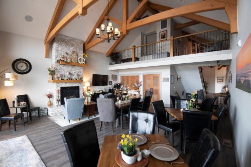 A spacious, modern living area with high wooden beams, a stone fireplace, and dining tables set for guests.