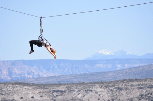 A person zip-lining over a mountainous landscape with snow-capped peaks in the background.