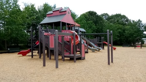 Colorful playground structure with slides and climbing areas, surrounded by trees and a sandy ground.