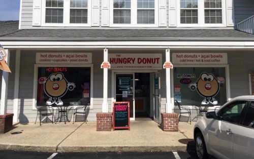 Exterior of The Hungry Donut shop featuring signage for hot donuts and acai bowls, with cartoon donut characters on windows.