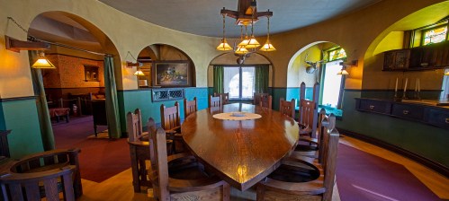 A spacious dining room with a large wooden table, arched doorways, and warm lighting, featuring rustic decor.