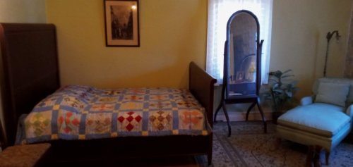 A cozy bedroom featuring a quilted bed, a mirror, a chair, and a framed picture on the wall.