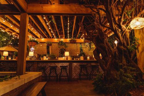 Cozy outdoor bar with wooden beams, string lights, and lush greenery, creating a warm, inviting atmosphere at night.