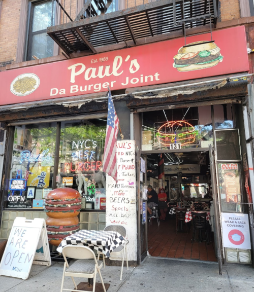 Exterior of Paul's Da Burger Joint, featuring a red sign, neon lights, and a large burger display. Open sign visible.