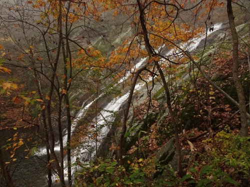 A serene waterfall cascades down rocky terrain, surrounded by autumn foliage and misty atmosphere.
