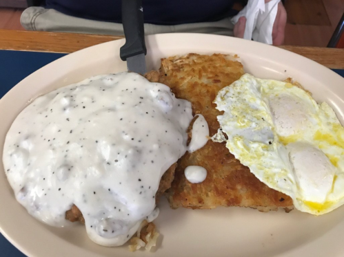 A plate of food featuring chicken fried steak with gravy, hash browns, and two sunny-side-up eggs.