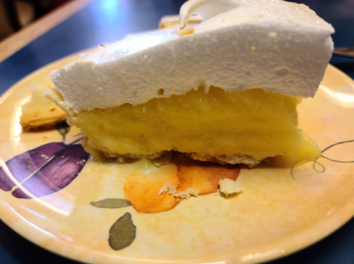 A slice of lemon meringue pie on a decorative plate, featuring a golden filling and fluffy white meringue topping.