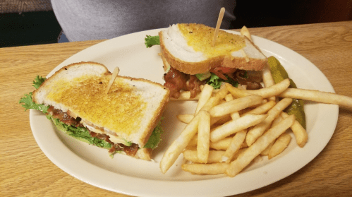A toasted sandwich with lettuce, tomato, and bacon, served with a side of French fries and a pickle on a plate.