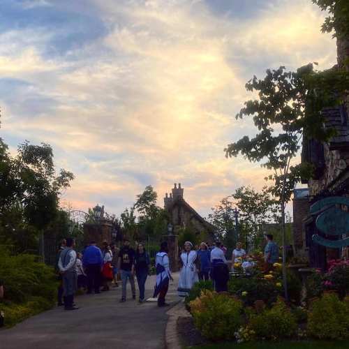 A scenic view of a park with people walking, lush greenery, and a colorful sky at sunset.