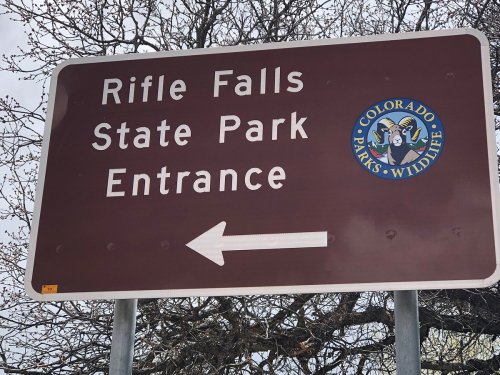 Brown sign indicating the entrance to Rifle Falls State Park, with an arrow pointing left. Colorado Parks & Wildlife logo included.