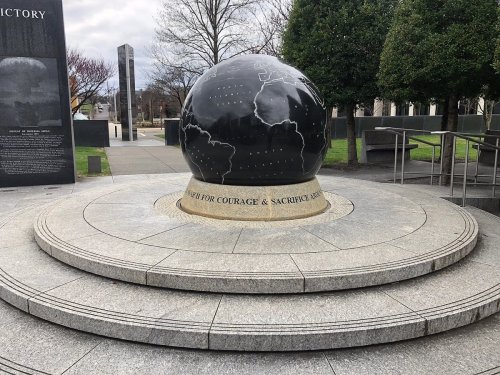 A black globe monument on a stone pedestal, surrounded by trees and a pathway, commemorating courage and sacrifice.