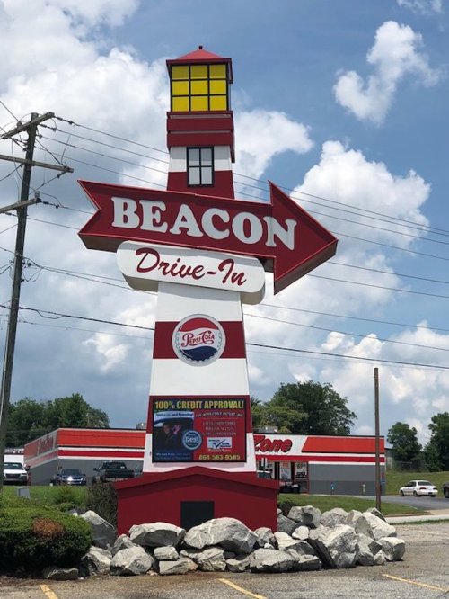 A tall, colorful sign for Beacon Drive-In featuring a lighthouse design, with a clear blue sky in the background.