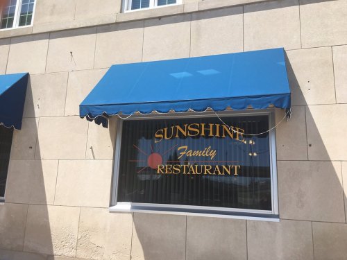 Blue awning above a window with the sign "Sunshine Family Restaurant" in gold lettering.